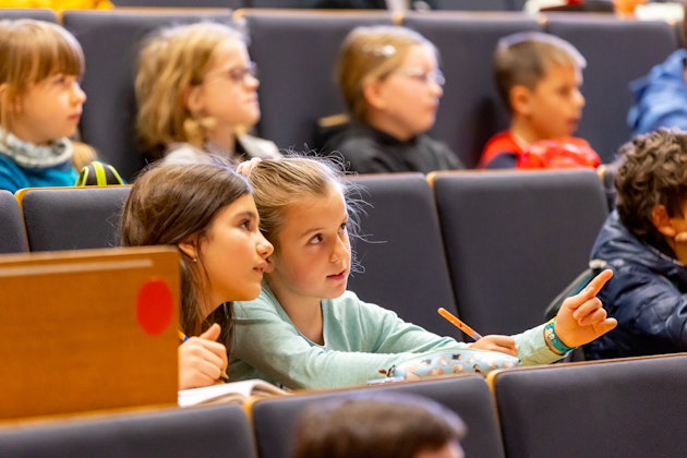Kinder in einem Hörsaal, zwei Mädchen sind im Fokus und schauen in die Ferne