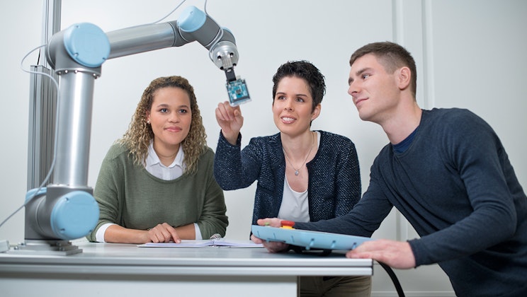 Zwei Studenten mit einer Dozentin an einem technischen Gerät, als Symbolbild für Hochschule Heilbronn