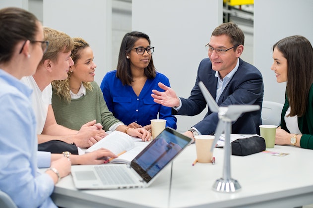 Ein Dozent erklärt fünf Studentinnen an einem Tisch etwas, als Symbolbild für Hochschule Heilbronn